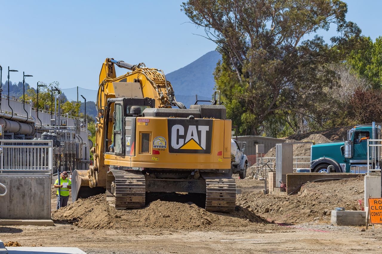 about-us-02 Excavator working at a construction site with mountains in the background.