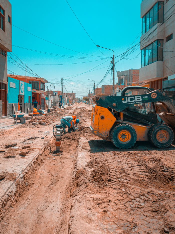 Busy urban road construction scene with workers and construction machinery under a bright blue sky.